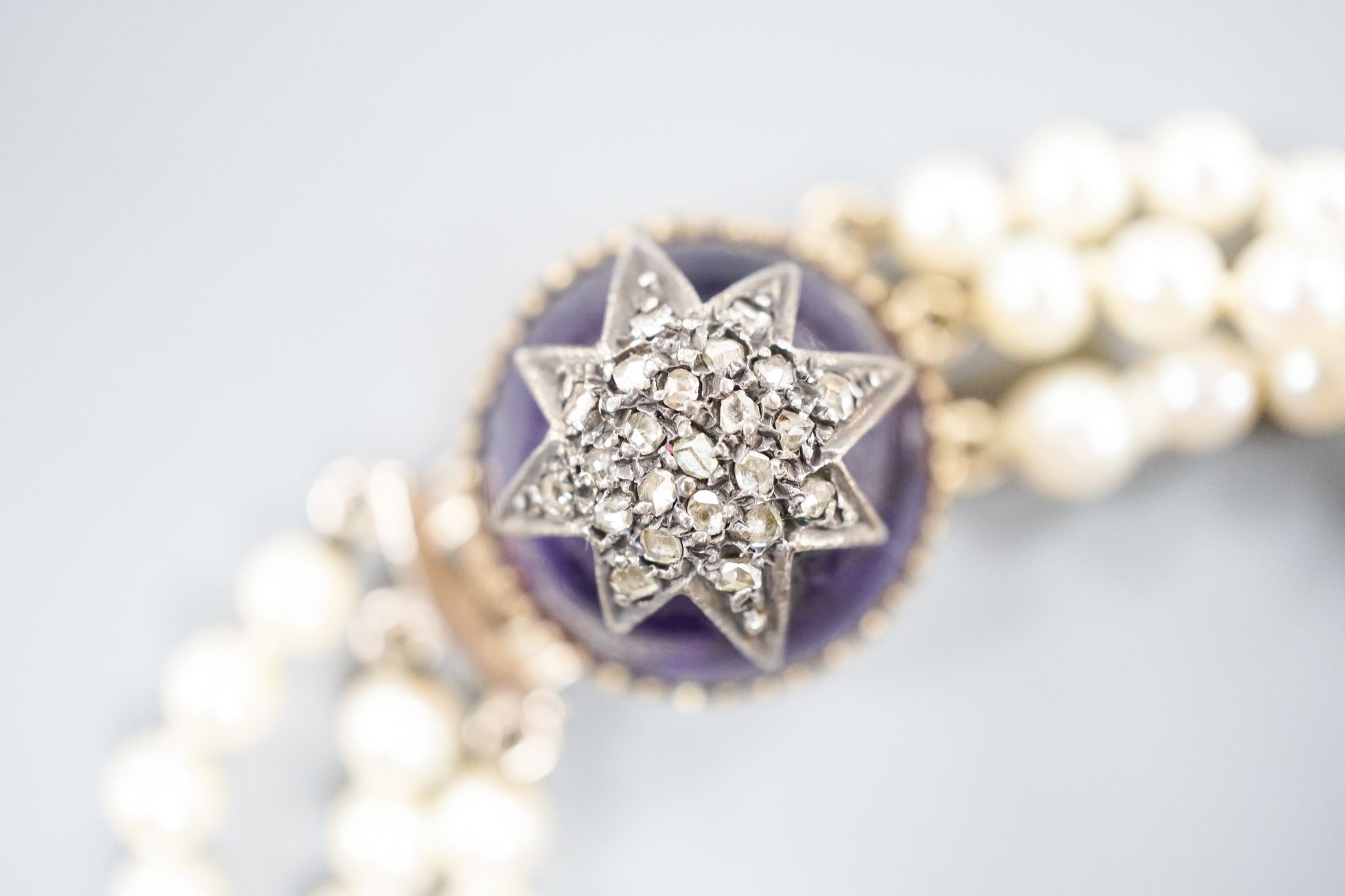 An early 20th century triple strand cultured? pearl bracelet, with rose cut diamond and cabochon amethyst set yellow metal clasp, 17.5cm, gross weight 21 grams.